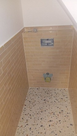 Badsanierung mit Feinsteinzeug in Terrazzo-Optik, Ziegelformat-Wandfliesen und Vorwand mit präzisen Gehrungsschnitten – für eine nahtlose, hochwertige Gesamtoptik.